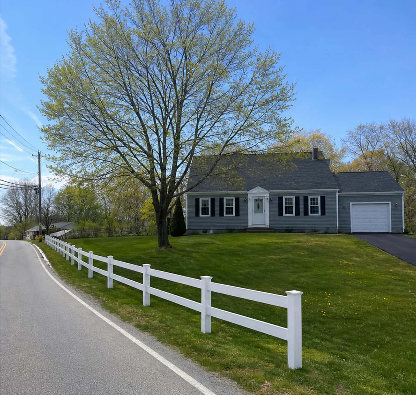 The same roadside in spring with a new white vinyl rail fence