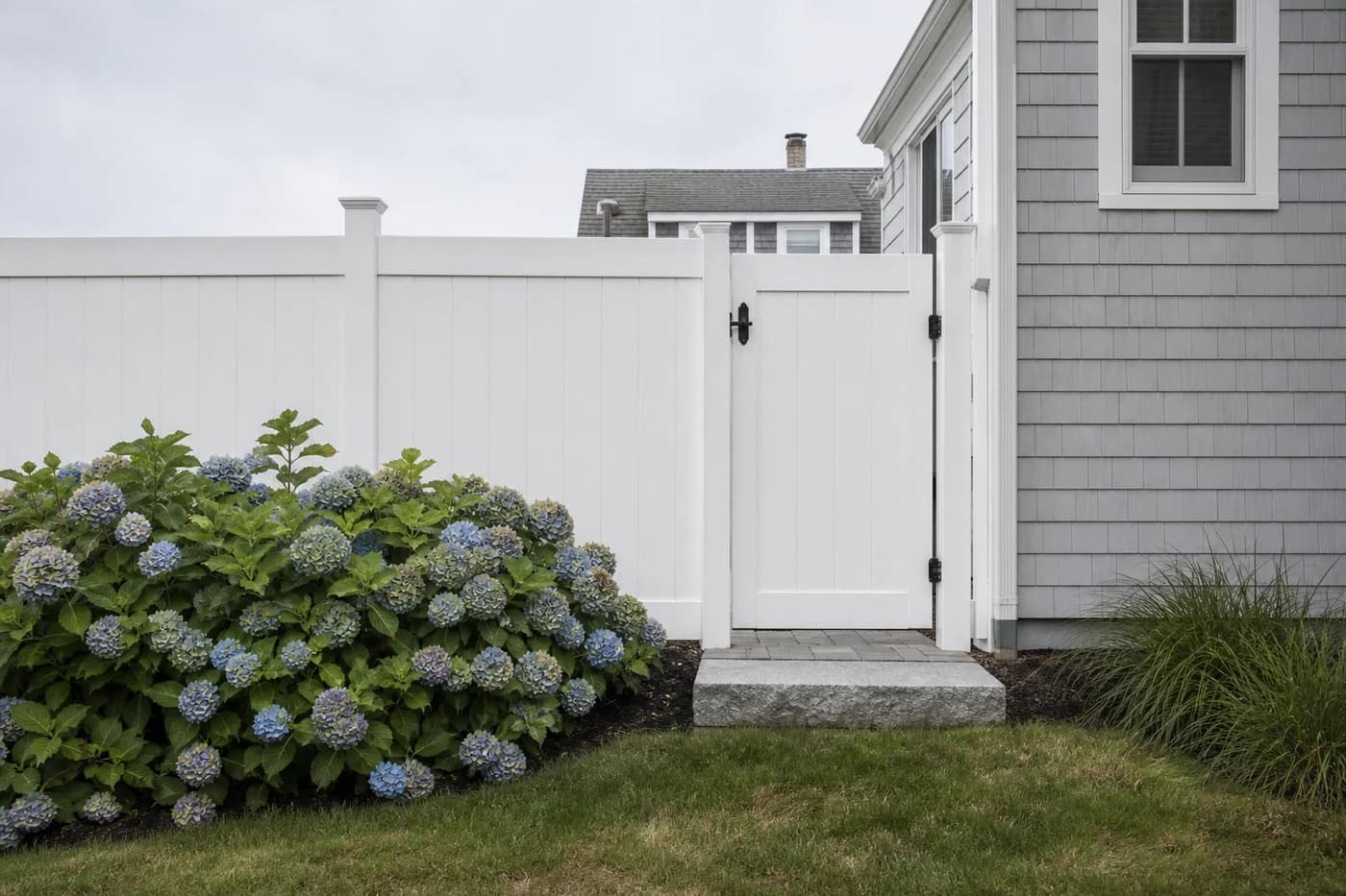 White vinyl privacy fence and gate beside hydrangeas and a shingled home